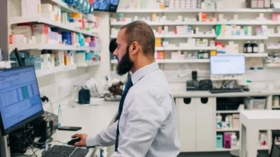 A man in a traditional NHS pharmacy working on a computer.