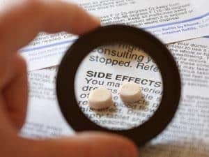 A person holding a magnifying glass over a pill.