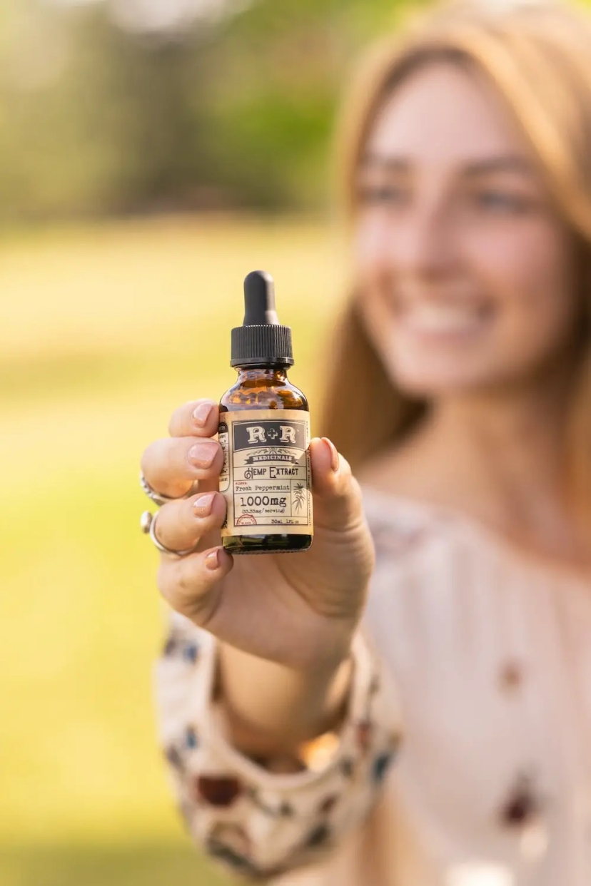 A woman holding up a small bottle of CBD oil for anxiety.