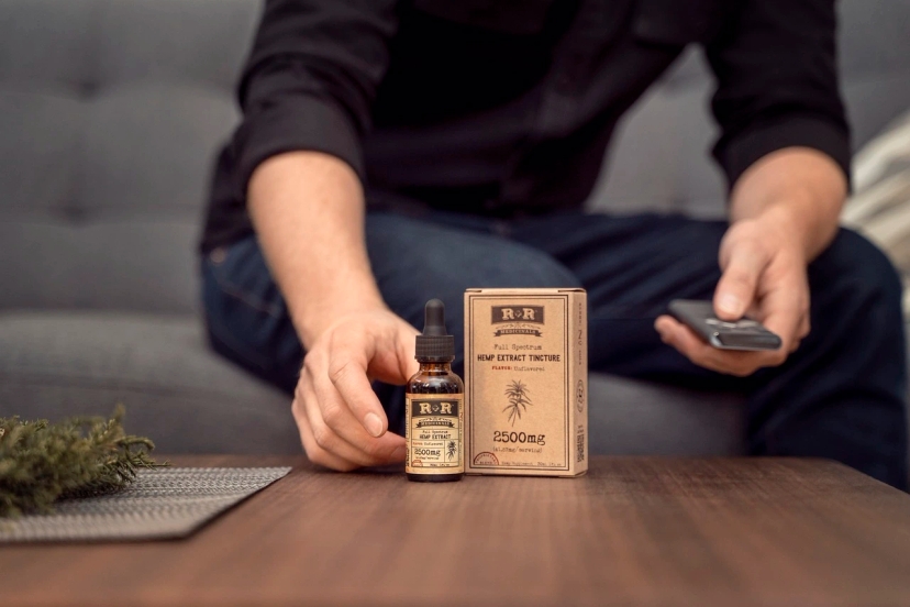 A man holding a remote next to a box of CBD oil for arthritis.