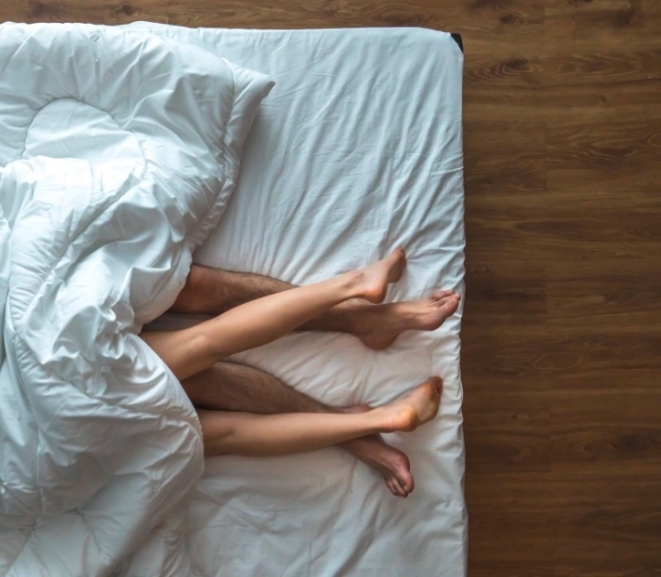 A couple is lying on a bed with white sheets, exploring questions about sex they recently googled.