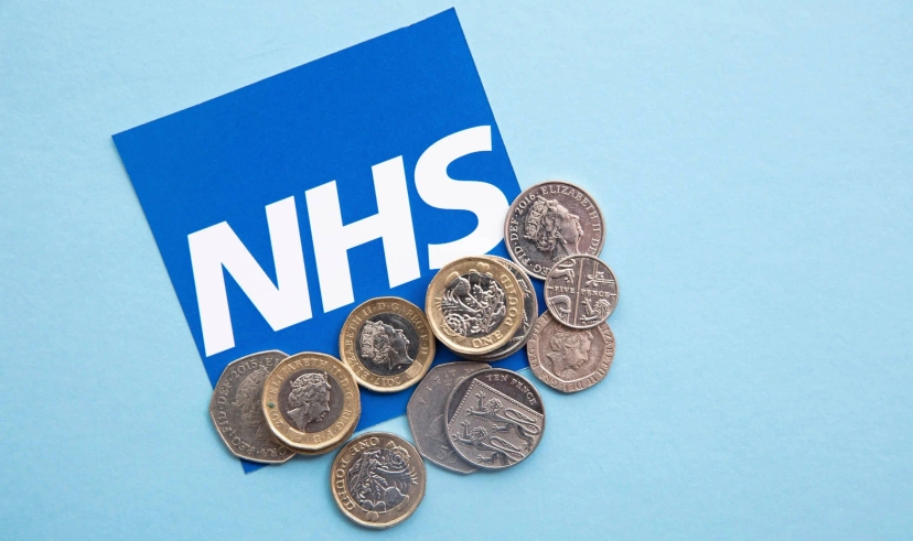 A stack of coins next to an NHS sign advertising A&E visit cost.