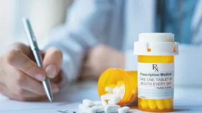 A doctor holding a prescription drug bottle and a pen, emphasizing savings for patients.