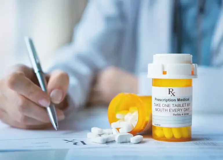 A doctor holding a prescription drug bottle and a pen, emphasizing savings for patients.