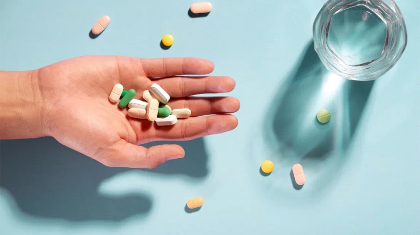 An emergency supply of medication, showcased by a hand holding pills and a glass on a blue background.