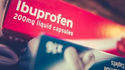 Close-up of a red box labeled "Ibuprofen 200mg liquid capsules," designed to help with stomach pain, partially overlapping a visible portion of another box of tablets in the foreground.