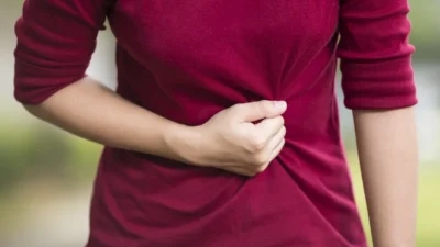 Person wearing a red shirt, holding their abdomen with one hand, possibly indicating symptoms of stomach pain or discomfort.