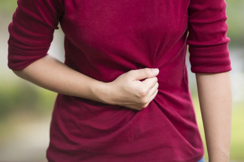 Person wearing a red shirt, holding their abdomen with one hand, possibly indicating symptoms of stomach pain or discomfort.