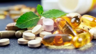 A variety of pills and capsules, including multicolored tablets and soft gel capsules, are scattered on a surface alongside fresh mint leaves, with some formulations that help manage sciatic nerve pain containing essential vitamins.