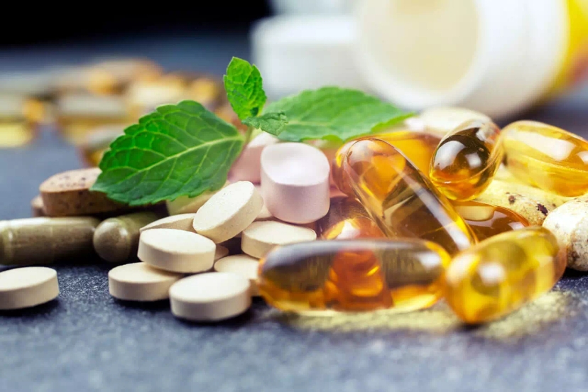 A variety of pills and capsules, including multicolored tablets and soft gel capsules, are scattered on a surface alongside fresh mint leaves, with some formulations that help manage sciatic nerve pain containing essential vitamins.