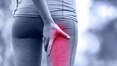 A person in athletic wear holds the back of their upper thigh, highlighted in red to indicate sciatic nerve pain or discomfort.