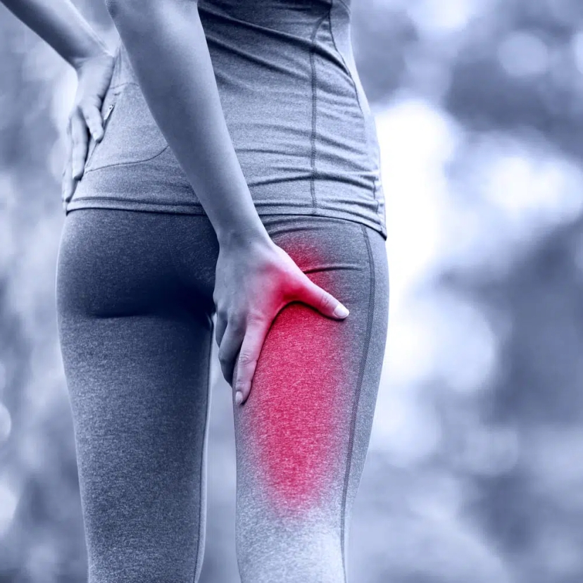 A person in athletic wear holds the back of their upper thigh, highlighted in red to indicate sciatic nerve pain or discomfort.