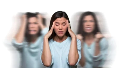 oman with a distressed expression, holding her head, with blurred images of herself in the background, illustrating the confusion and hallucinations associated with psychotic disorders.