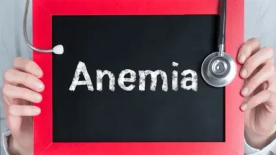 A person holds a small chalkboard with the word "Anemia" written on it, and a stethoscope draped on the side of the board, symbolizing the importance of finding an anemia cure.