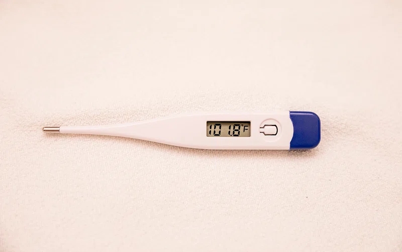 A digital thermometer displaying a temperature reading of 101.8°F, indicating a fever, lays on a light-colored surface.