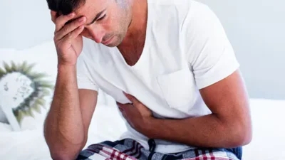 Man sitting on a bed, holding his stomach in pain, representing the question "Can you die with Crohn's disease?" and the severity of its symptoms.