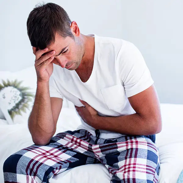 Man sitting on a bed, holding his stomach in pain, representing the question "Can you die with Crohn's disease?" and the severity of its symptoms.