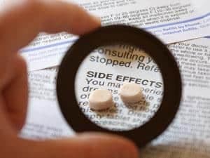 A person holding a magnifying glass over a pill.