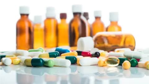 Various pills and capsules are scattered on a surface with multiple amber prescription bottles standing upright in the background, perhaps indicating treatments for an upper respiratory infection.