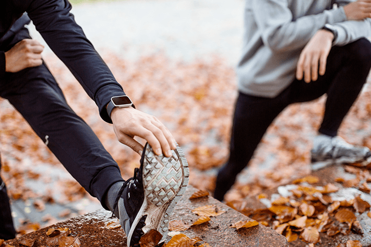 Two people benefiting from the positive effects of running while tying their shoes in the fall.