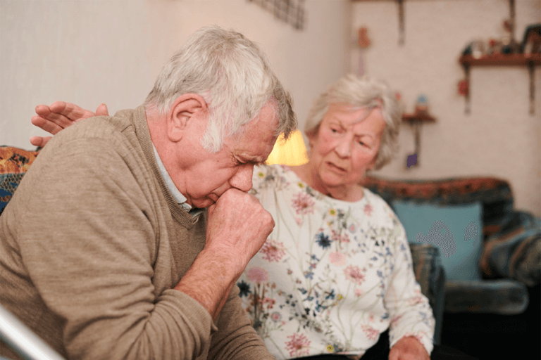 An older couple practicing social distancing on a couch during coronavirus.