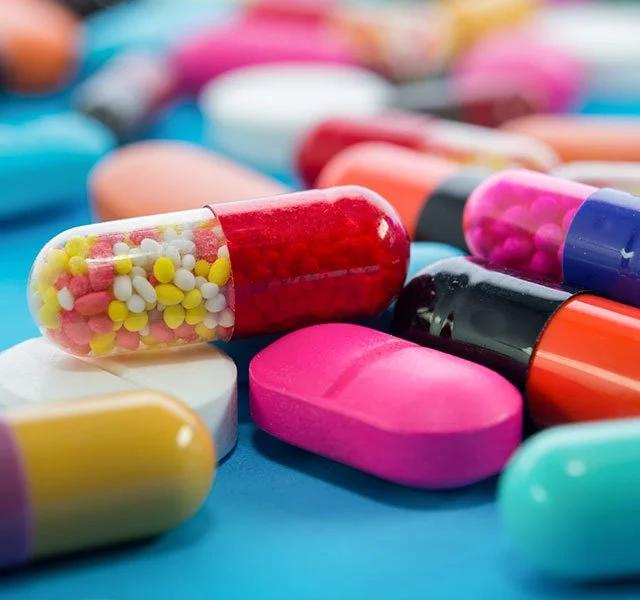Many colorful pills and capsules medication on a blue background.