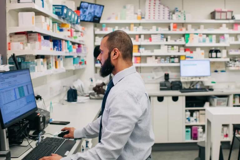 A man in a traditional NHS pharmacy working on a computer.