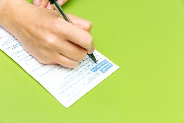 A person writing on a piece of paper with a pen, possibly indicating important notes for free prescriptions or PIP eligibility.