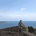 Person standing on a stone ledge with a scenic ocean view in the background, showcasing their amazing weight loss transformation under a clear blue sky.