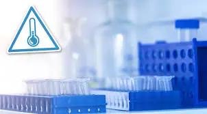 A lab setting with test tubes in racks and a temperature warning sign on the left, crucial for maintaining cold chain integrity in refrigerated drug shipping.