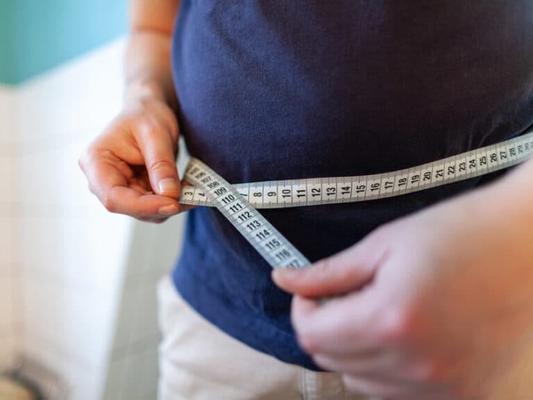 Person measuring their waist with a tape measure to determine the Amycretin dosage.