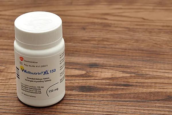 A bottle of Wellbutrin XL 150 mg extended-release tablets on a wooden surface, known to cause weight loss.