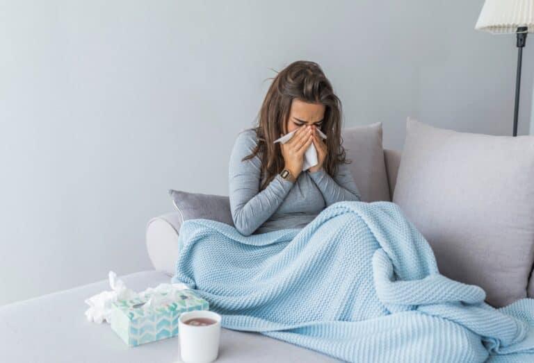 A woman is sitting on a couch, wrapped in a blanket, with a cup of coffee, battling the flu.