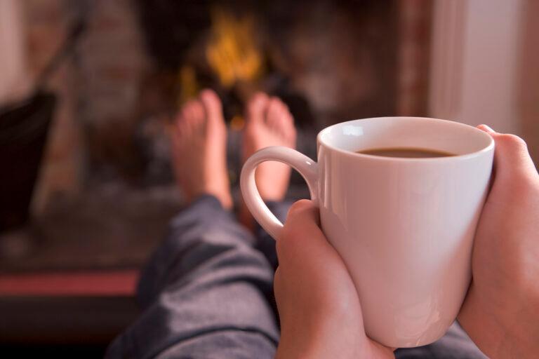 A sober individual enjoying a cup of coffee in front of a warm fireplace.