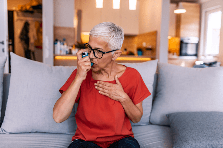 A woman is sitting on a couch with her hands on her chest, displaying signs of asthma.