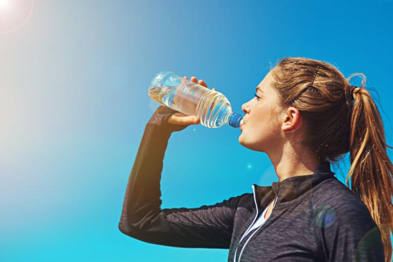 A woman partaking in Dry January drinking water from a bottle on a sunny day.