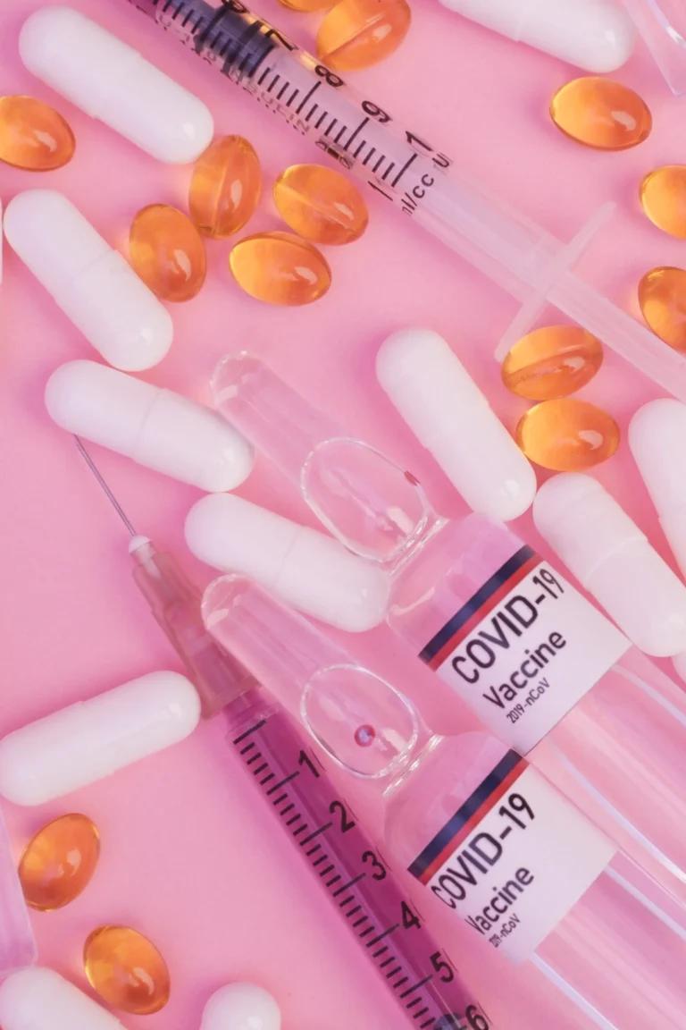 Syringes filled with vitamins and Wegovy pills on a pink background.