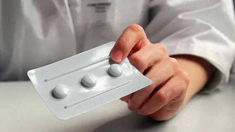 A person is holding a white pill on a table.