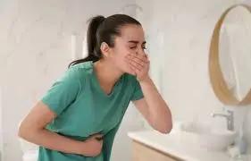 Woman in a green shirt holding her stomach and covering her mouth about to vomit
